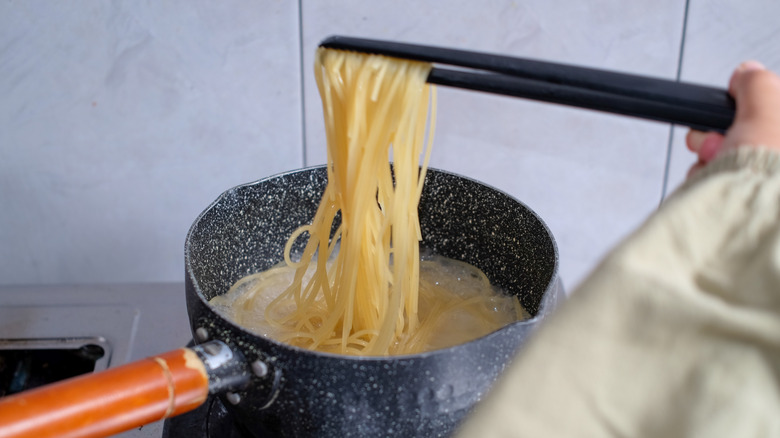 A chopstick scooping cooked noodles out of a pot with boiling water