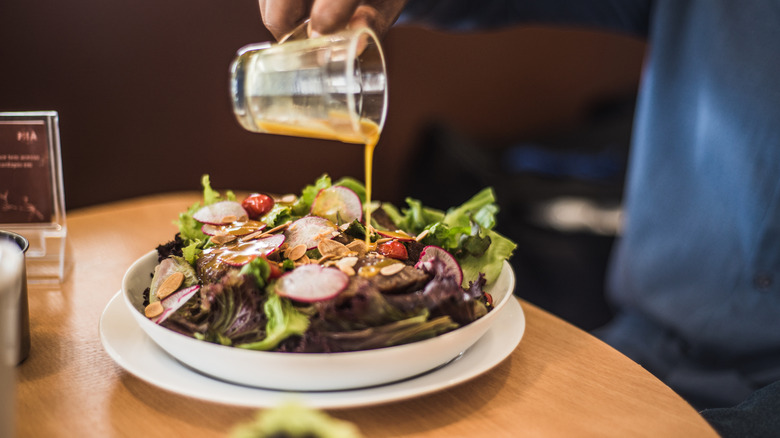 An individual pouring vinaigrette over a fresh salad