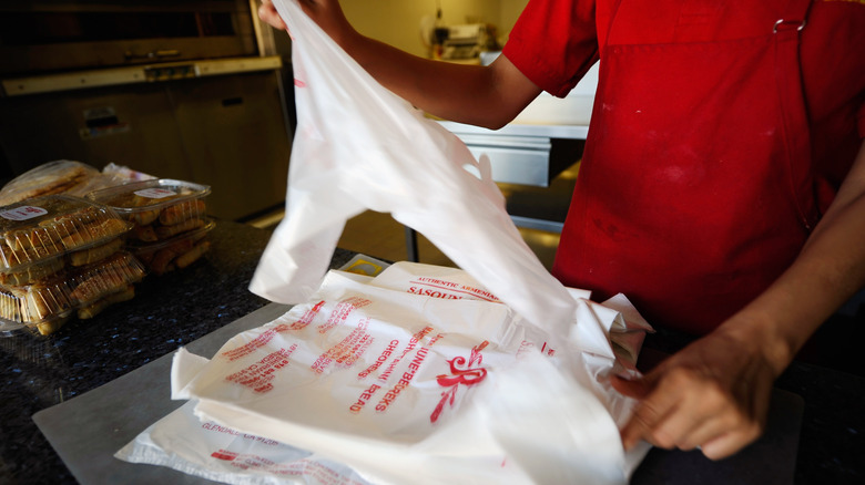 A bakery worker pulling a plastic grocery-style bag off of a stack of bags, ready to bag purchases.
