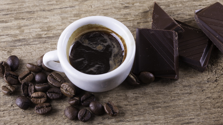A cup of espresso next to coffee beans and chopped chocolate