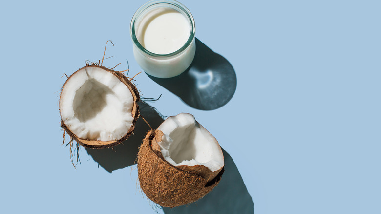 Coconut halves next to a glass of coconut milk