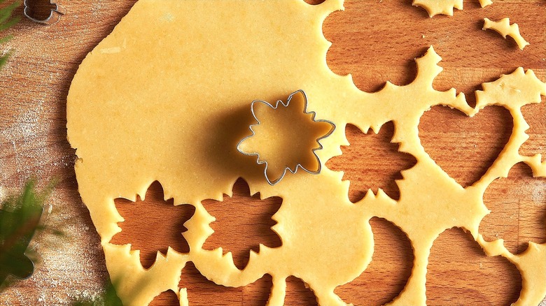 Snowflake cookie cutter in raw pie dough on wood surface