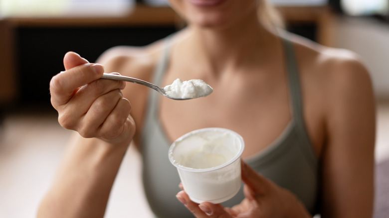 Woman scooping yogurt out of a clear cup.