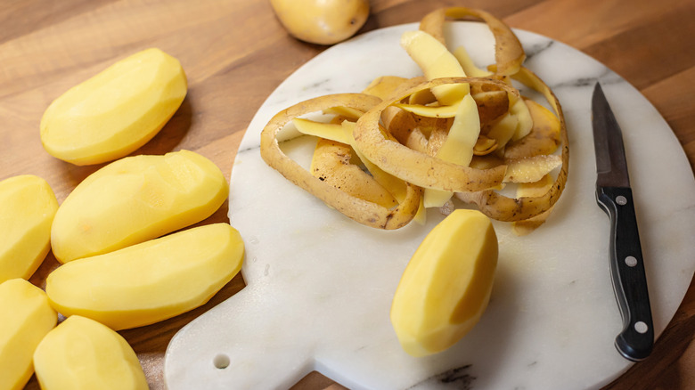 Potato peels on a cutting board with a knife and peeled potatoes