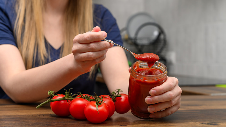 An illustrative image showing a woman holding a jar of tomato jam.