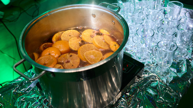 A stainless steel pot simmering sliced tangerines and cloves on a stovetop.