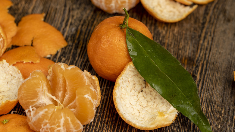 A tangerine with peels on a wooden surface.