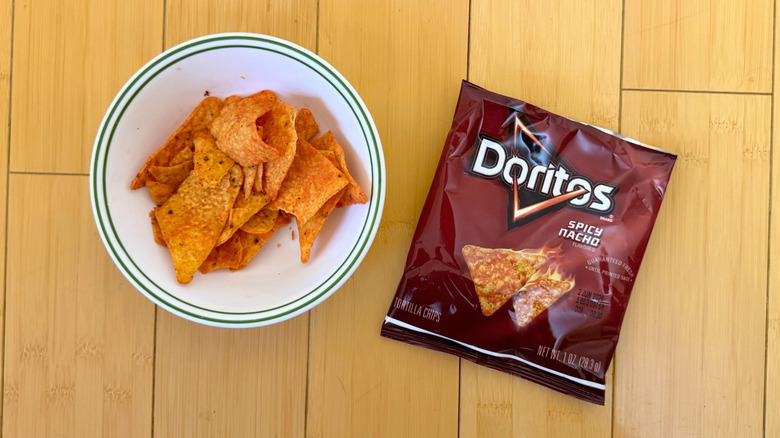 Bag of Spicy Nacho Doritos beside filled bowl of chips