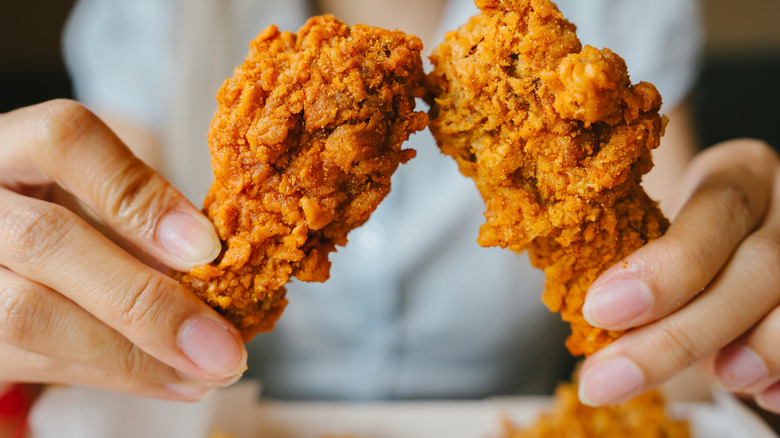 A woman holding two pieces of crispy fried chicken.