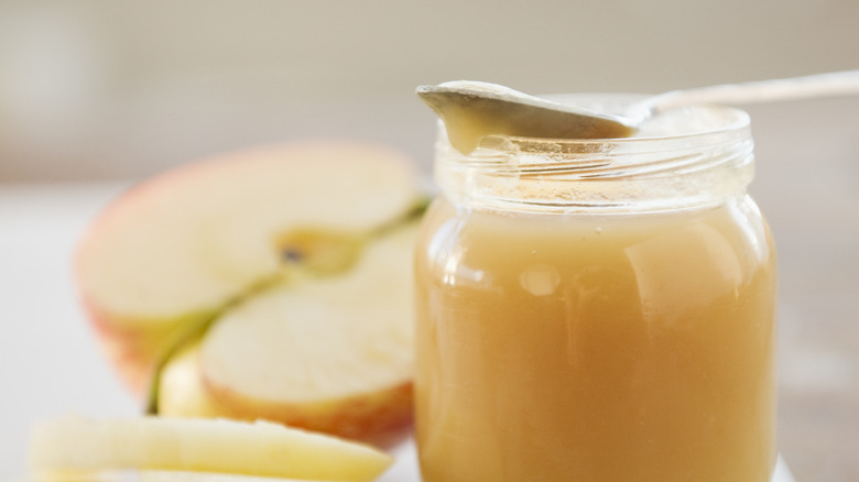 Jar of applesauce with spoon surrounded by apples