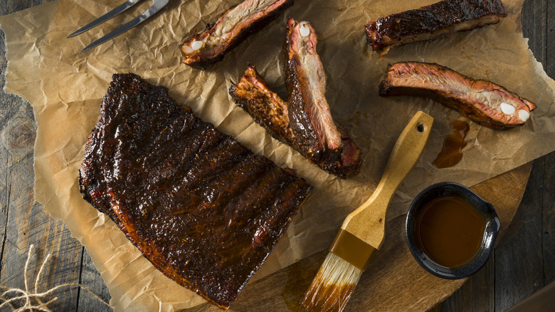 BBQ baby back ribs on parchment paper with sauce and brush on the side