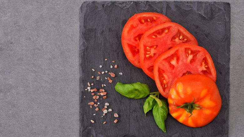 A sliced tomato on a wooden board beside a small pile of fancy salt.