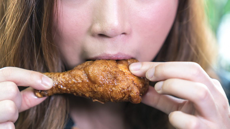 A person taking a bite of a chicken wing drumette