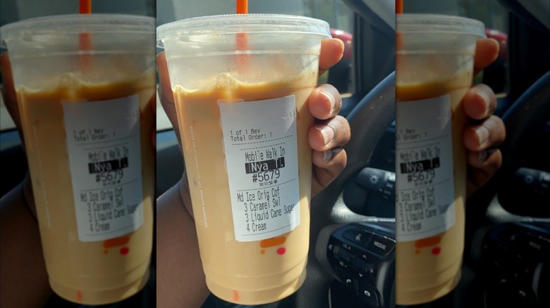 Woman's hand holding a Dunkin' iced coffee with liquid cane sugar listed on the drink label.