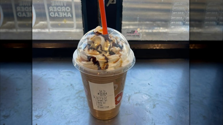 Dunkin' iced coffee siting on a table topped with whipped cream, caramel, and mocha drizzle.