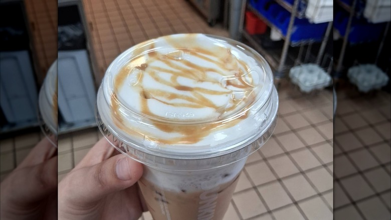 Person holding an iced coffee topped with cold foam and a caramel drizzle.