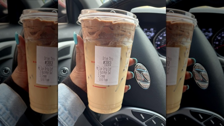 Woman's hand holding a Dunkin' iced coffee with cream and chocolate cold foam.