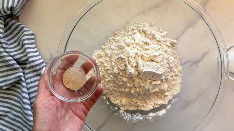 hand adding yeast to bowl of flour