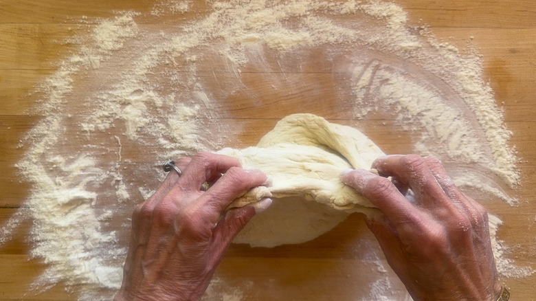 hands folding dough on floured surface