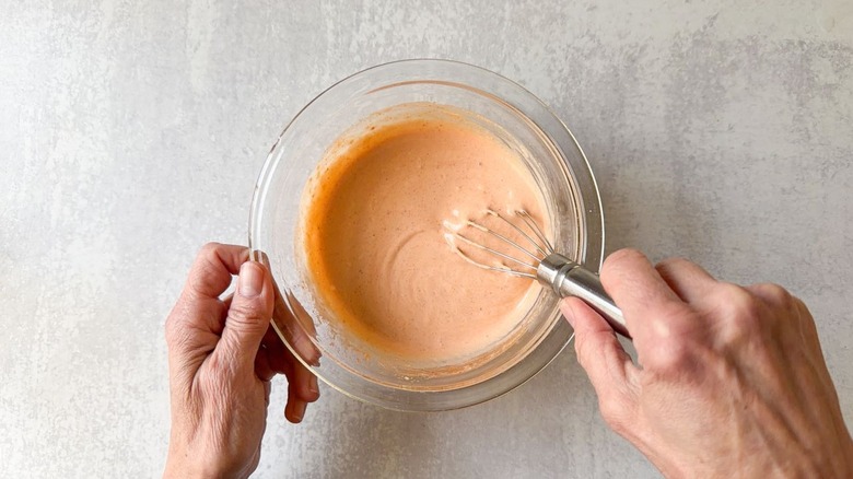 Whisking dynamite sauce in a glass bowl