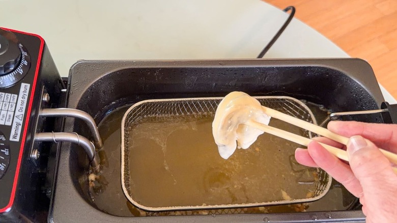 Lowering battered shrimp into hot oil in fryer using chopsticks