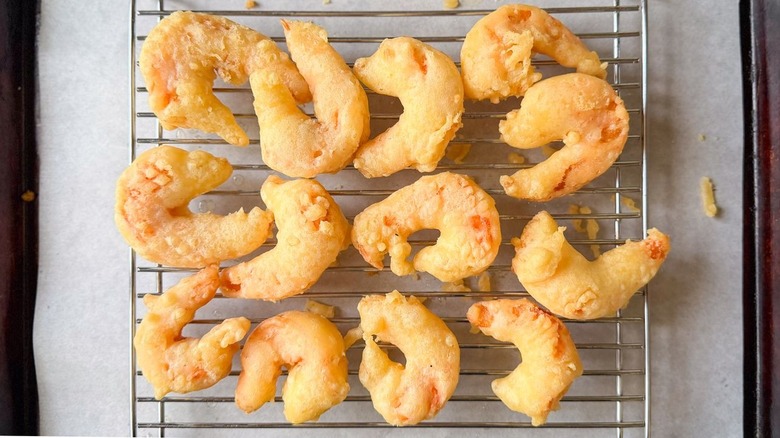 Battered and fried shrimp on rack set over parchment-lined baking sheet