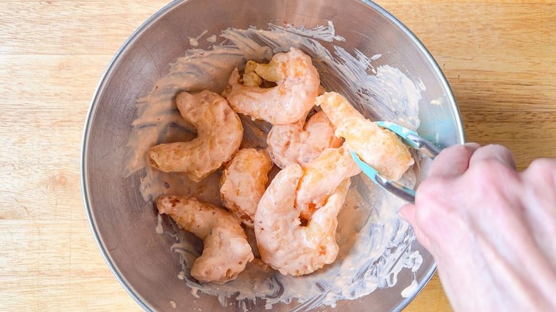 Tossing battered and fried shrimp with dynamite sauce in a stainless steel bowl with tongs