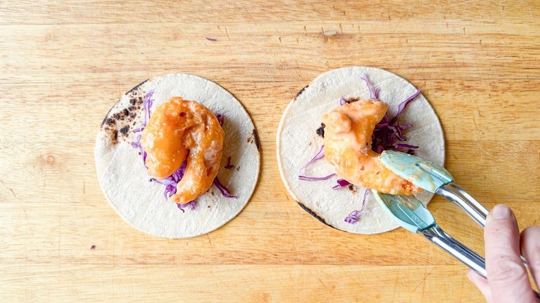 Placing dynamite shrimp on purple cabbage in corn tortillas