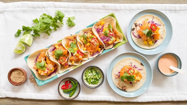 Dynamite shrimp tacos on platter and plates with garnishes and dynamite sauce