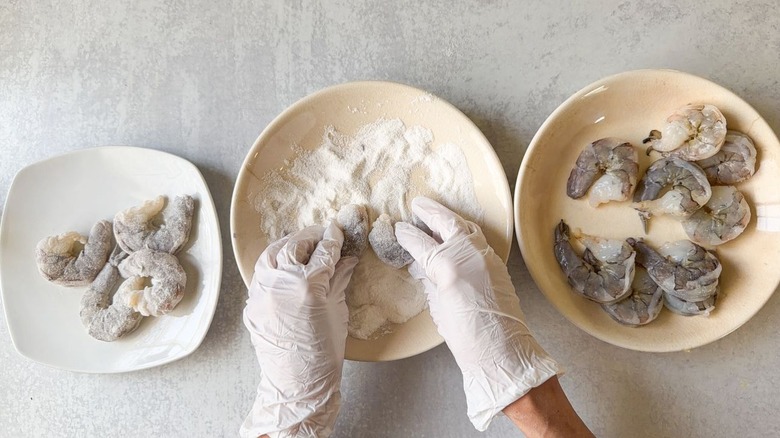 Dredging jumbo shrimp in cornstarch in a bowl wearing gloves