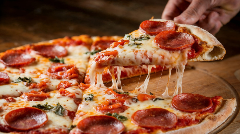 Pepperoni pizza slice being lifted from wooden board