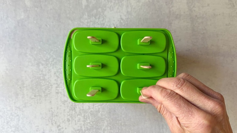 Inserting wooden sticks into green popsicle mold