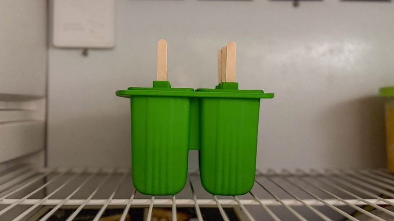 Green popsicle mold with sticks in freezer