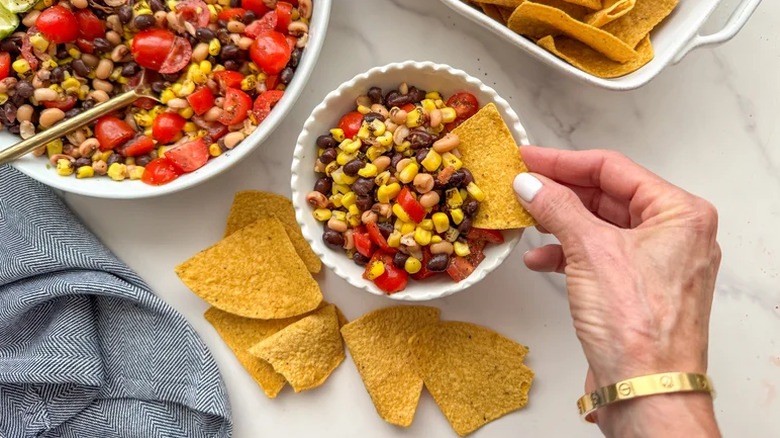 Hand scooping cowboy caviar out of a bowl with chips.