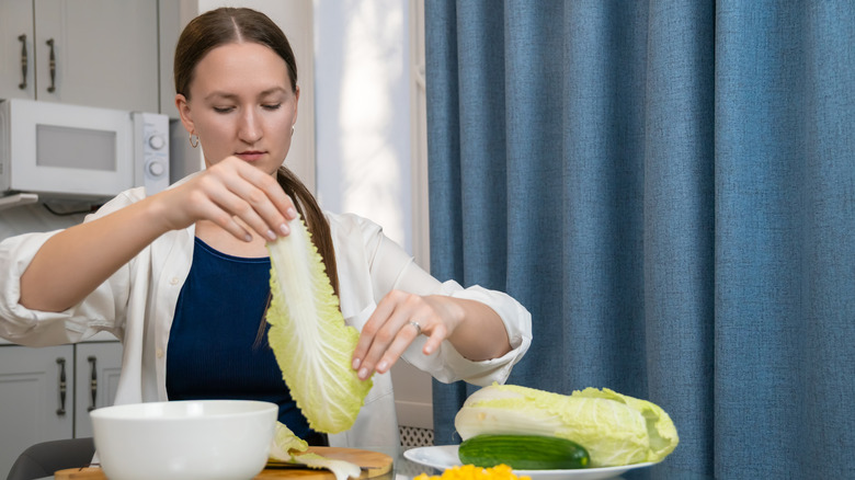 Young woman holding leaf of cabbage to make stuffed Napa cabbage rolls.