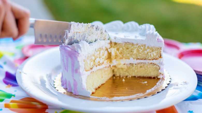 A knife slicing through vanilla layer cake with white icing