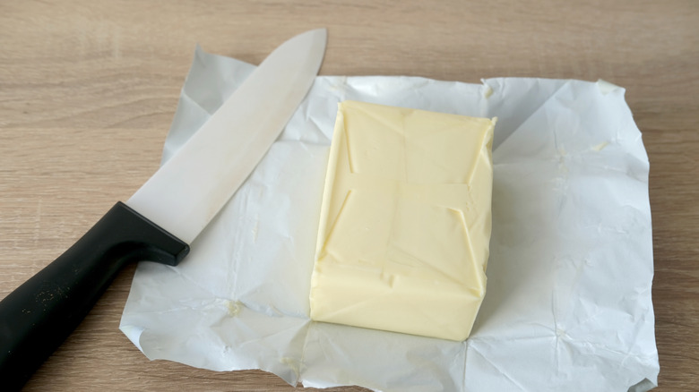 a knife with a black handle laying on a butter wrapper, next to a block of butter