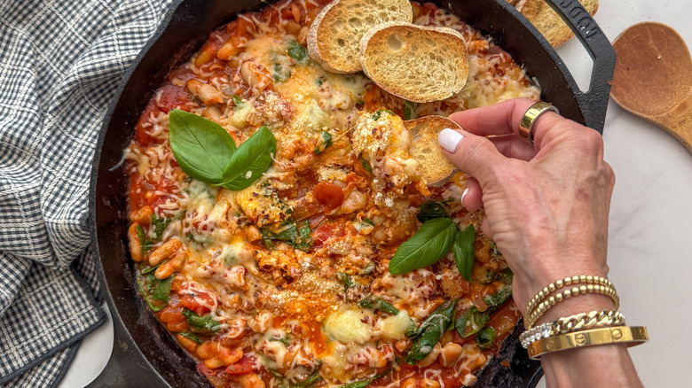 Hand dipping baguette slice into pizza bean skillet
