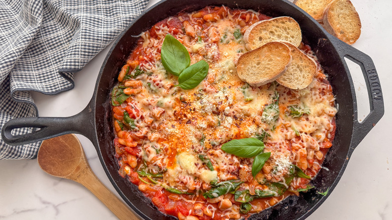 Cheesy pizza beans in skillet with basil and toasted baguette slices