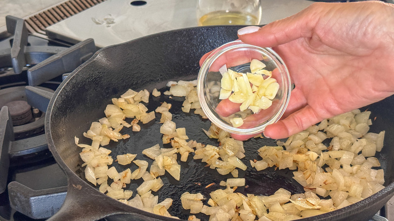 hand adding garlic to pan with onions