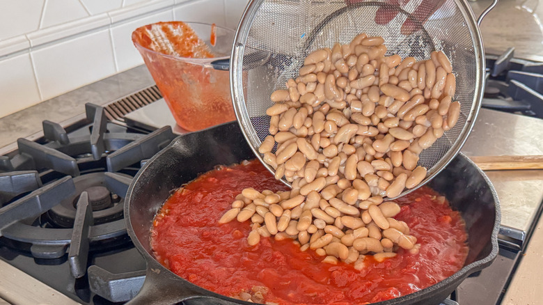 Pouring white beans into pan with marinara sauce