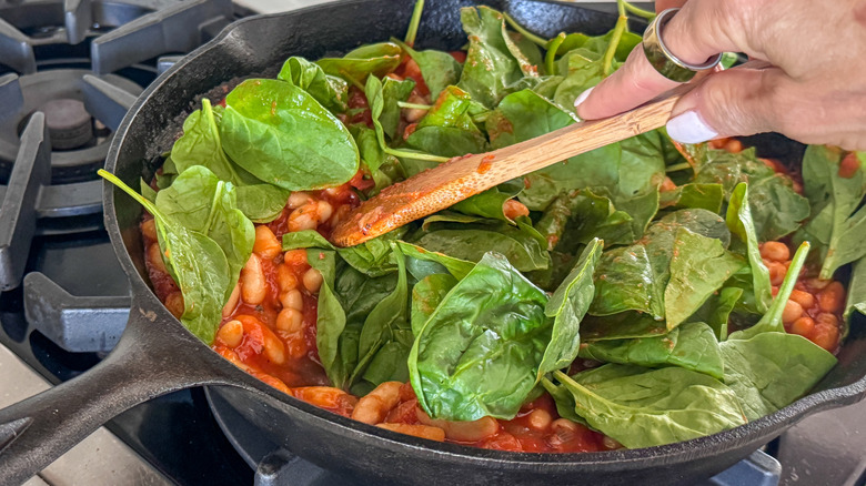 hand stirring spinach in pan