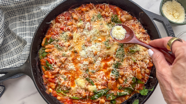Hand sprinkling parmesan over bean skillet