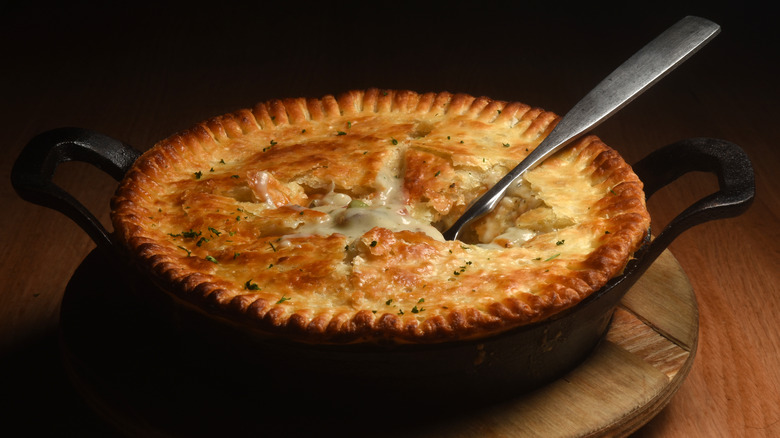 Chicken pot pie in cast iron with a serving utensil stuck through the top crust