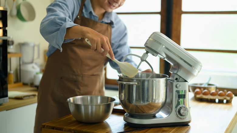 A baker using a rubber spatula to scrape the inside of a mixing bowl