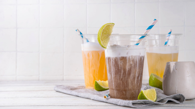 Assorted dirty soda drinks in plastic cups with blue and white striped straws