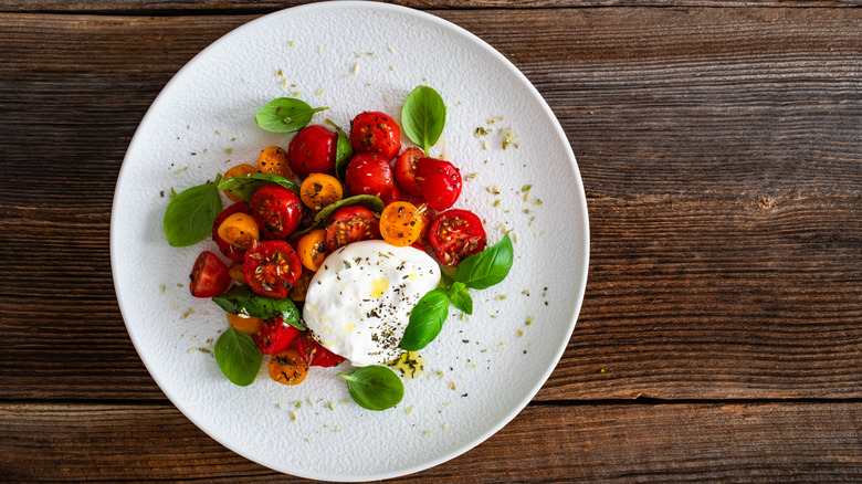 Burrata and fresh tomatoes on a plate on a wooden cutting board.