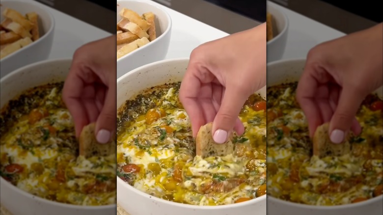 Woman dipping crostini into burrata cheese dip.