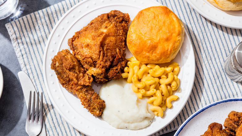 Fried chicken on a white plate with mashed potatoes, macaroni and cheese, and a biscuit.
