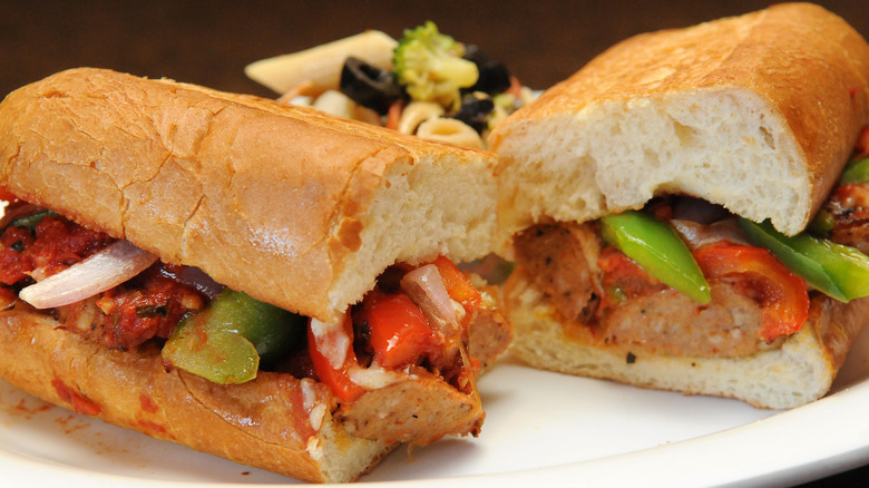 Sausage, peppers, and onion sub cut in half on a white plate